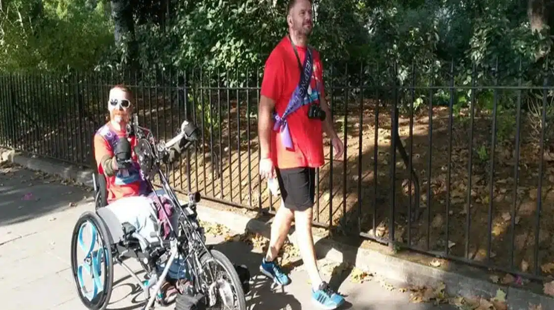 A man and woman walking on a pavement with a wheelchair.